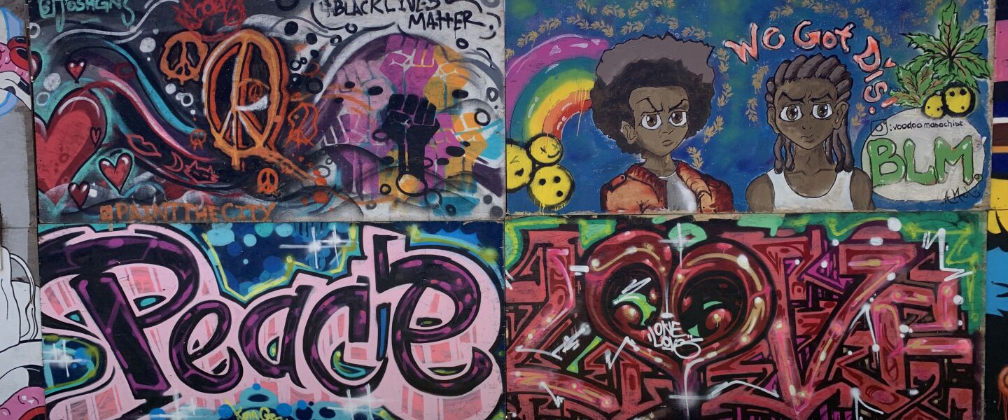 A cluster of murals promoting love and peace, including one at the top left by artist Joshua “SNAGZ” Valdovinos and one at the top right by the artist who goes by Voodoo Masochist and that reads, “We Got Dis!”