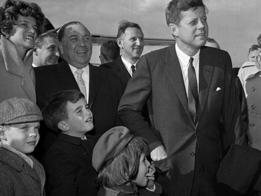 In this April 28, 1961, photo, President John F. Kennedy stands during a welcoming ceremony at O’Hare Airport as Mayor Richard J. Daley looks on, with Kennedy’s sister Eunice Kennedy Shriver, at left, and some of her children. | AP