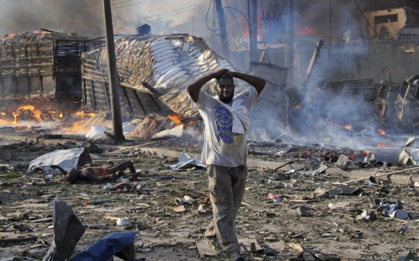 A Somali gestures as he walks past a dead body, left, and destroyed buildings at the scene of a blast in the capital Mogadishu, Somalia Saturday, on Oct. 14, 2017. | Farah Abdi Warsameh/AP photo