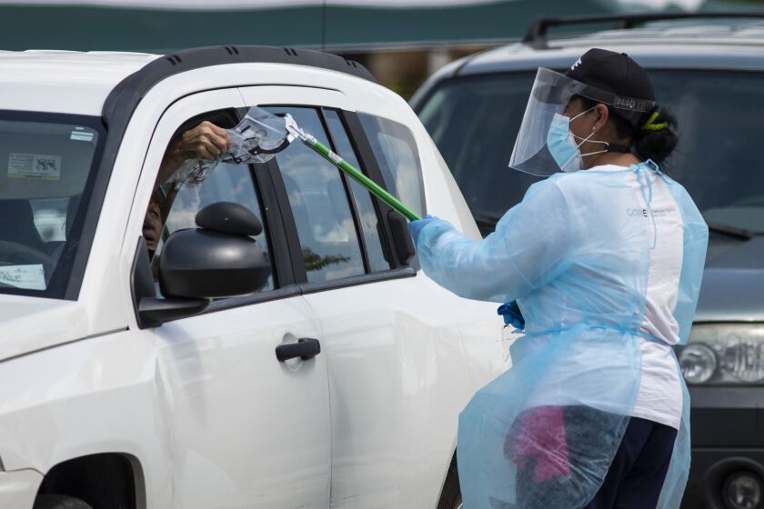 Testers use grabbing tools to administer swabs to people getting tested for COVID-19 at the drive-thru portion of a one-day testing site arranged by the Community Organized Relief Effort at St. Mary Star of the Sea School on July 29.