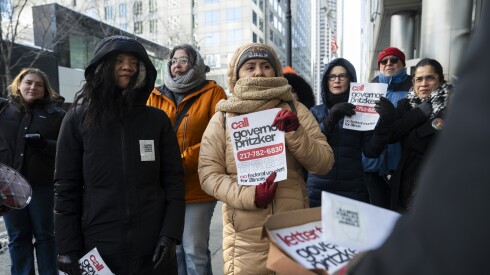 A group of protestors wearing winter jackets and scarves stands outside a government building to deliver letters.